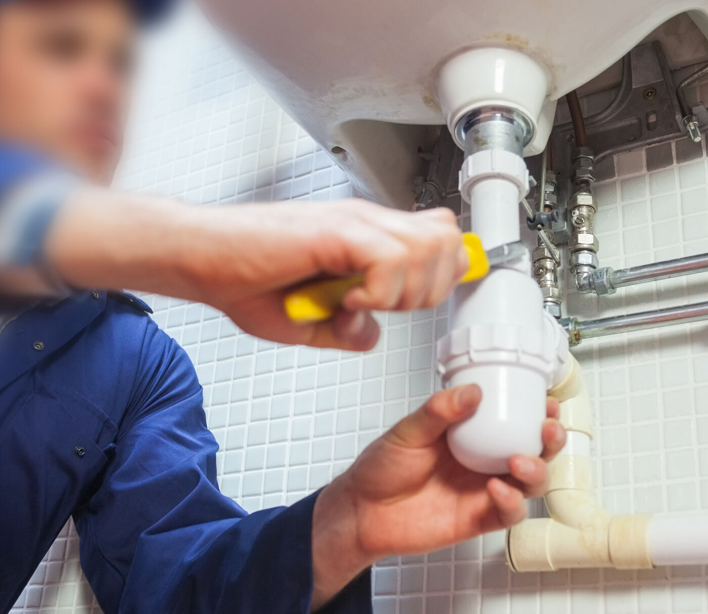 Plumber fitting a waste trap under a basin